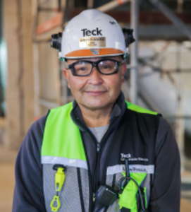 A worker wearing a hard hat, safety glasses, and a high-visibility vest in a work environment.
